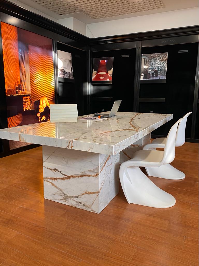Contemporary boardroom featuring a Dekton Awake marble-effect table with gold veining, designer white chairs, and a luxury commercial interior.